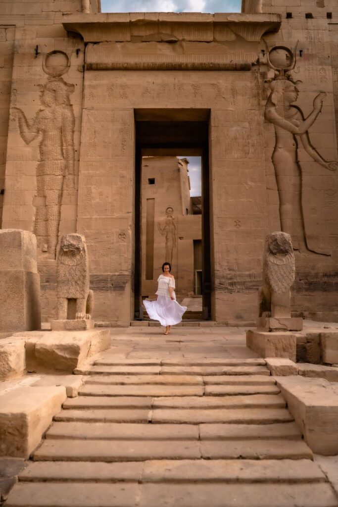 A woman in a flowing white dress walks through the monumental doorway of an ancient Egyptian temple lined with carved statues. A serene and safe moment that captures Egypt solo female travel in one of the safest places for solo female travelers.