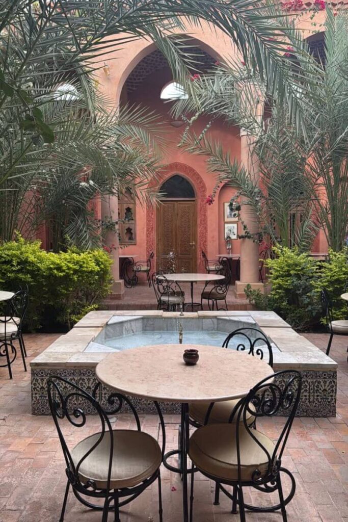 A tranquil café courtyard in Egypt with a small fountain, arched doorways, and wrought-iron chairs surrounded by palm trees. One of the safest places for solo female travelers to unwind and enjoy the slower side of Egypt travel for women.