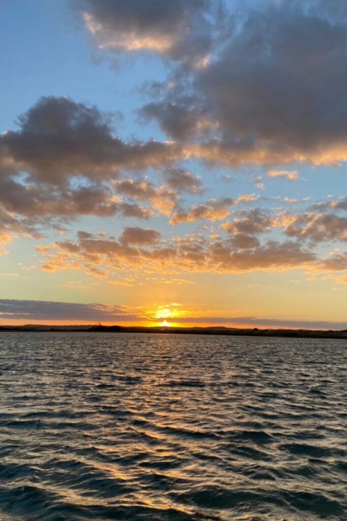 Bright sunset over a rippling lake in Siwa Oasis, Egypt, with golden clouds glowing above the horizon—ideal for representing the serene siwa lakes and natural beauty of this Egyptian oasis.