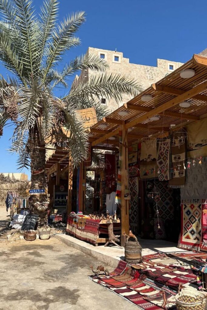 Outdoor dining area with bamboo tables and chairs in front of a mud-brick hotel in Siwa Oasis, Egypt, under clear blue skies—capturing the peaceful charm of a hotel in siwa and siwa oasis hotels.
