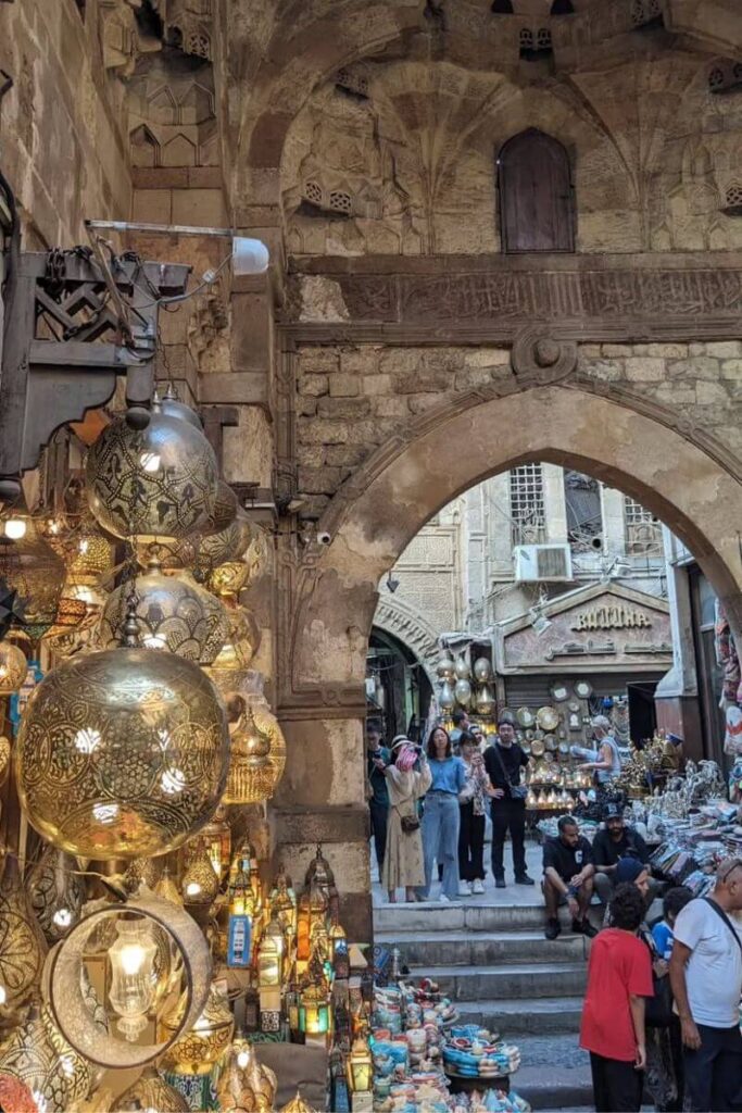 Bustling marketplace in Cairo with brass lanterns and souvenir stalls under Mamluk architecture, a cultural gem near the temple of Cairo and a glimpse into modern life around Egypt's historic sites.