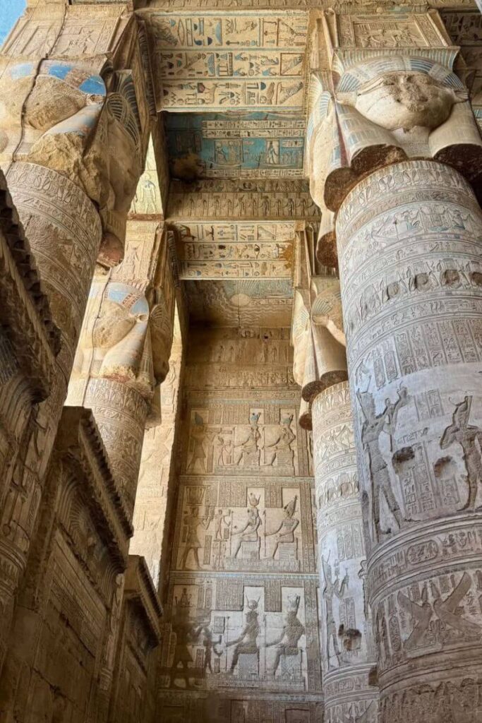 Richly decorated blue and tan ceilings of Dendera Temple with towering columns, covered in hieroglyphs and images of deities—representing detailed architecture of Egypt and temples of ancient Egypt.