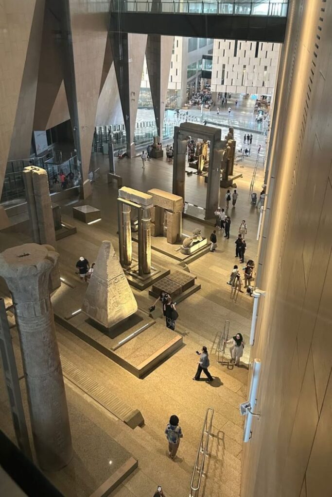 Modern interior of the Grand Egyptian Museum with massive ancient artifacts and visitors exploring. A major Egyptian landmark and one of the best places to visit in Egypt with family.