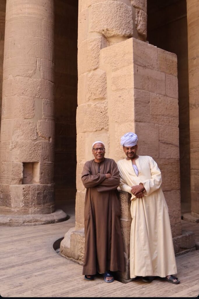 Two men in traditional Egyptian robes near ancient stone pillars — tipping in Egypt often includes local staff at temples and historical sites. Use this tipping guide for Egypt travel.
