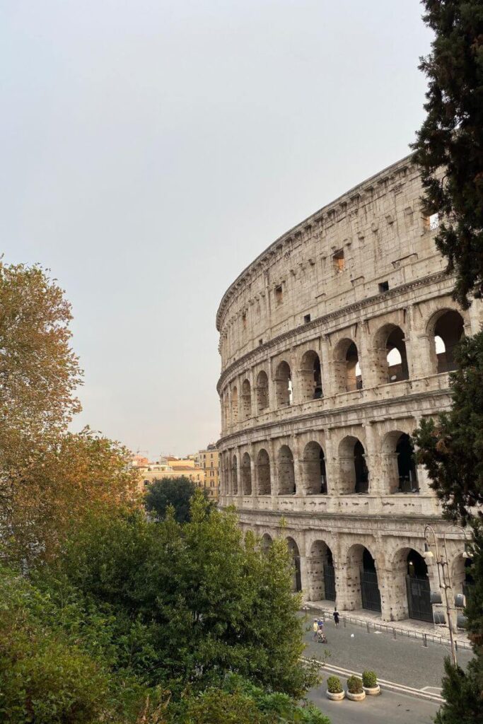 The iconic Colosseum rises above treetops in Rome, one of the best cities to travel solo in Europe. A classic highlight for solo female travel in Italy, traveling to Rome alone, and Europe solo travel destinations.