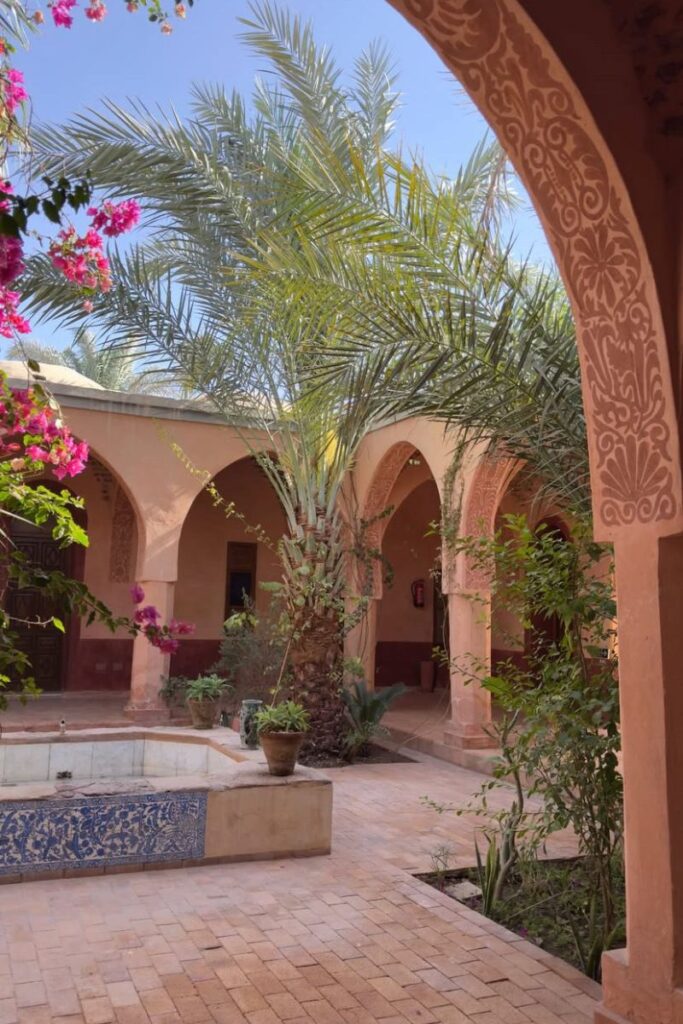 A serene courtyard with archways, palm trees, and a small tiled fountain surrounded by flowering plants. A great escape for women travelers in Egypt looking for the safest places for solo female travelers to relax.