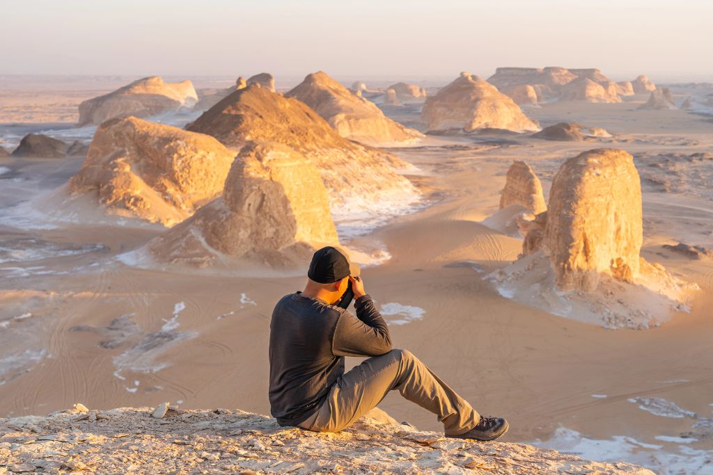 Traveler photographing surreal white rock formations in the White Desert at golden hour. One of the most beautiful and unusual places to visit in Egypt for nature lovers.