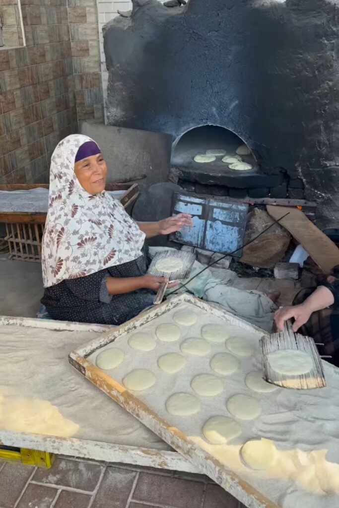 Elderly Egyptian woman baking flatbread in a traditional oven – an authentic cultural moment for those interested in things to know about Egypt, tipping in Egypt, and what to take to Egypt for a deeper travel experience.