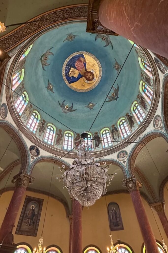 The domed ceiling of a Coptic church in Cairo is painted with saints, angels, and a central image of Christ, with a grand chandelier hanging below. A cultural gem included in many itinerary for Egypt plans and Egypt travel itinerary stops.