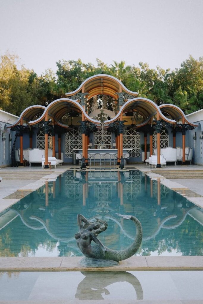 A luxurious pool scene featuring a mermaid statue and ornate architecture surrounded by palm trees. Swimsuits with modest cover-ups should be included in your Egypt packing list, especially if you're staying in upscale resorts or planning on relaxing by the pool.