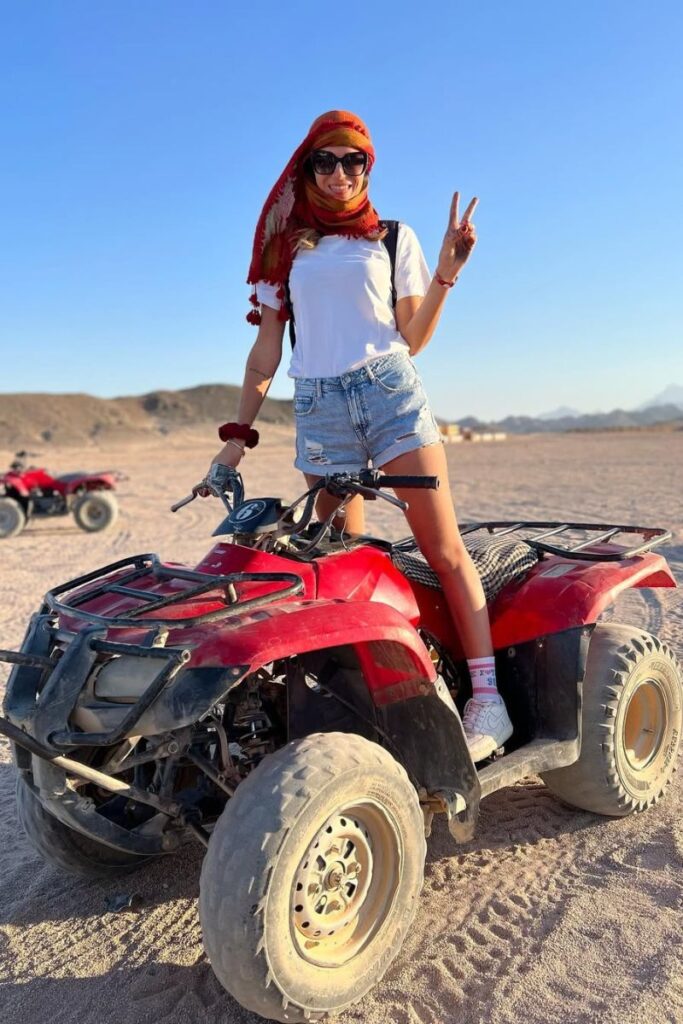 Adventurous woman standing on a red ATV bike in the Egyptian desert during golden hour. ATV tours are fun activities to do in Egypt and perfect for couples seeking unique experiences in Egypt.
