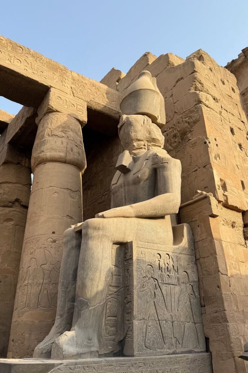 Seated stone statue of a pharaoh at Luxor Temple, surrounded by hieroglyphs and ancient columns bathed in late afternoon sun. A stunning moment in any itinerary Egypt 10 days or Egypt travel plans to Luxor.