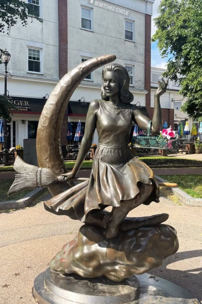 A bronze statue of Samantha Stephens riding a broomstick in front of a crescent moon, located in Salem, Massachusetts, making it a must-see stop on a Halloween trip to Salem for fans of witches and pop culture.