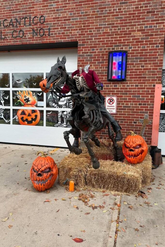 A life-size headless rider holding a jack-o’-lantern while mounted on a skeletal horse, displayed with carved pumpkins outside a building, representing one of the best places to go for Halloween in the United States.