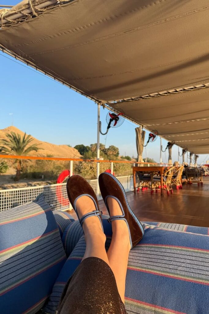 Feet propped up on a Nile cruise deck with striped pillows and scenic desert and palm trees in the background. A relaxing moment typical of a slow-paced 10 day Egypt itinerary or luxury Egypt travel plans.
