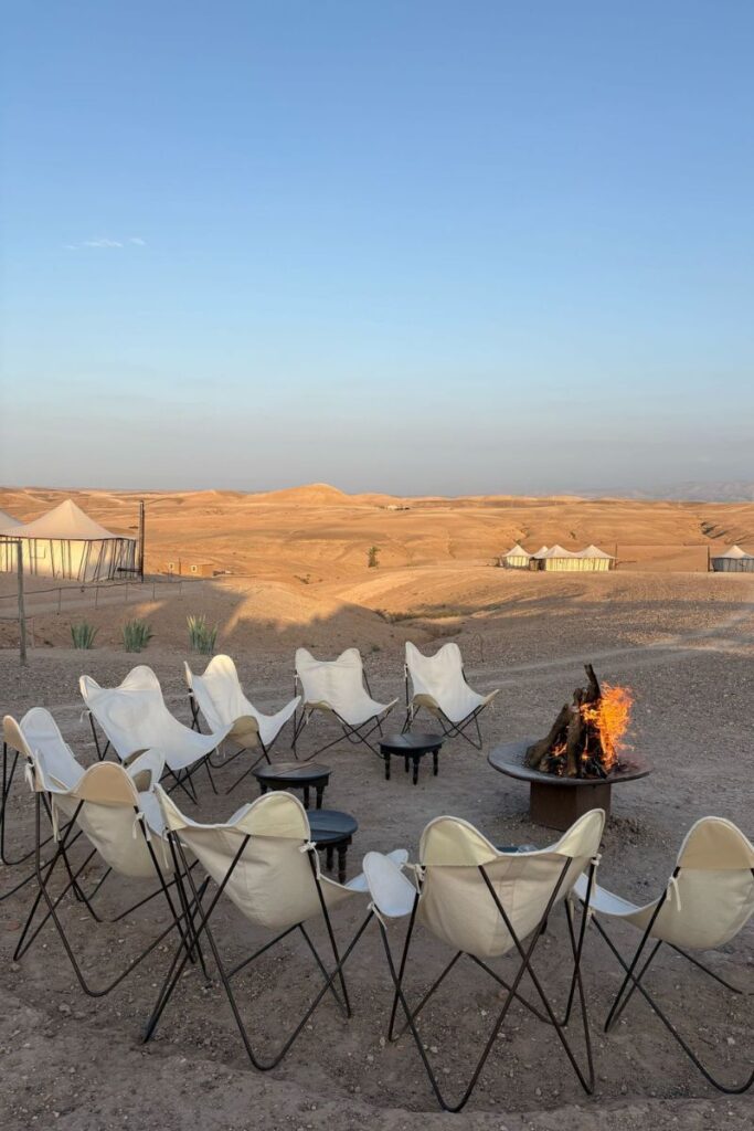 A circular setup of white canvas chairs surrounds a fire pit in a golden desert glamping site at sunset. One of the warmest destinations in October, this spot is perfect for travelers wondering where is warm in October for a unique and peaceful retreat.