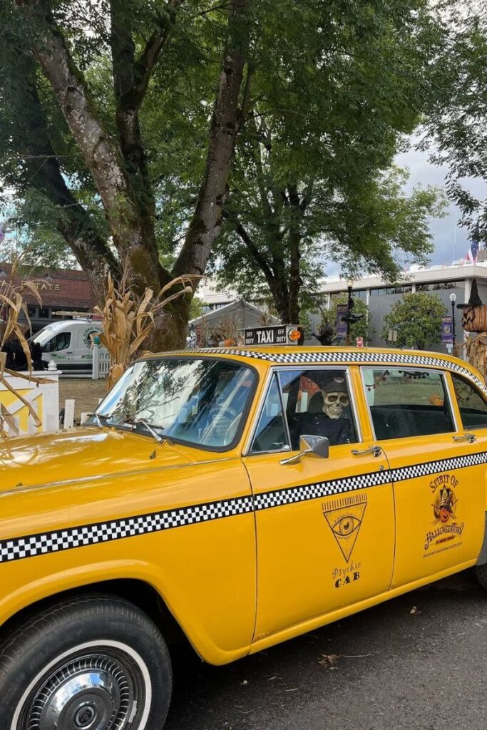 A bright yellow vintage taxi labeled “Psychic Cab” with a skeleton driver sits decorated for Halloween, adding quirky charm to one of the fun places to visit for Halloween in the US.