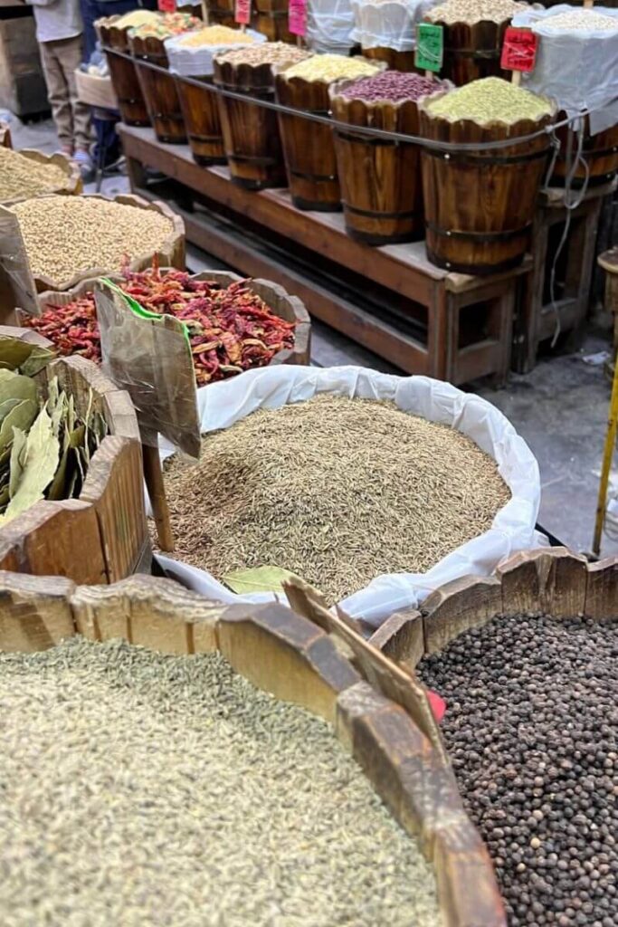 Close-up of a traditional Egyptian spice market with large wooden barrels filled with cumin, pepper, bay leaves, and chili peppers. Wandering through this vibrant market is one of the top things to do in Hurghada town and a flavorful addition to your Hurghada travel guide.