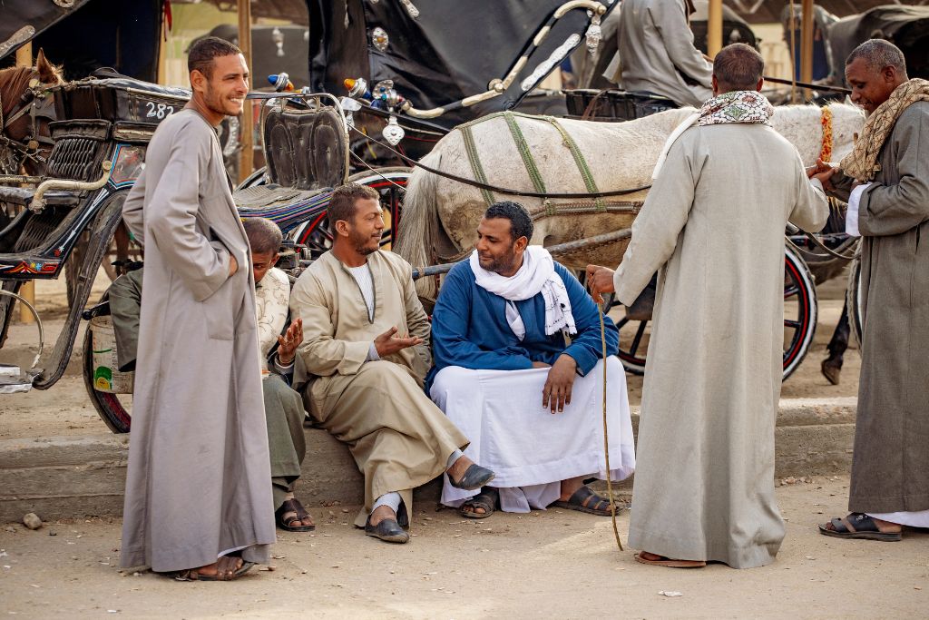 Group of local Egyptian men sitting and chatting near horse-drawn carriages. Offers insight into everyday Egyptian life – ideal for travelers wanting to understand local culture and receive travel tips for Egypt beyond tourist sites.
