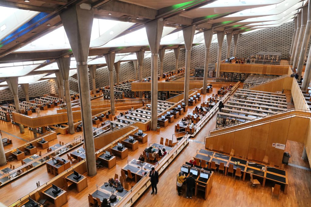 Wide view of the modern and spacious Bibliotheca Alexandrina filled with reading desks, natural light, and angular architecture. Exploring this cultural hub is one of the most unique things to do in Egypt and a great non-touristy thing to do in Egypt.