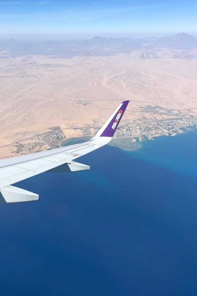 Aerial view from a plane window showing the Red Sea’s vivid blue waters and the desert coastline near Hurghada. The photo captures the excitement of arrival and hints at the best time to visit Hurghada and how accessible Hurghada travel guide adventures can be.