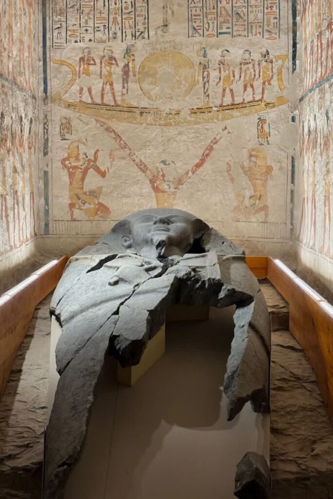 A massive cracked sarcophagus rests in a richly painted tomb covered in ancient Egyptian art and hieroglyphs. Supportive shoes and breathable clothing are must-haves on any packing list for Egypt and essential when visiting tombs and temples.