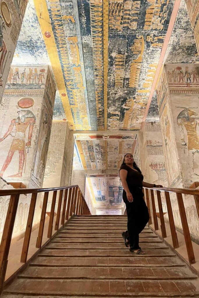 A tourist ascending stairs beneath a vividly painted ceiling full of hieroglyphics in a royal tomb in Luxor. Tomb exploration here is one of the best activities in Egypt and a deeply immersive Egypt experience for history lovers.