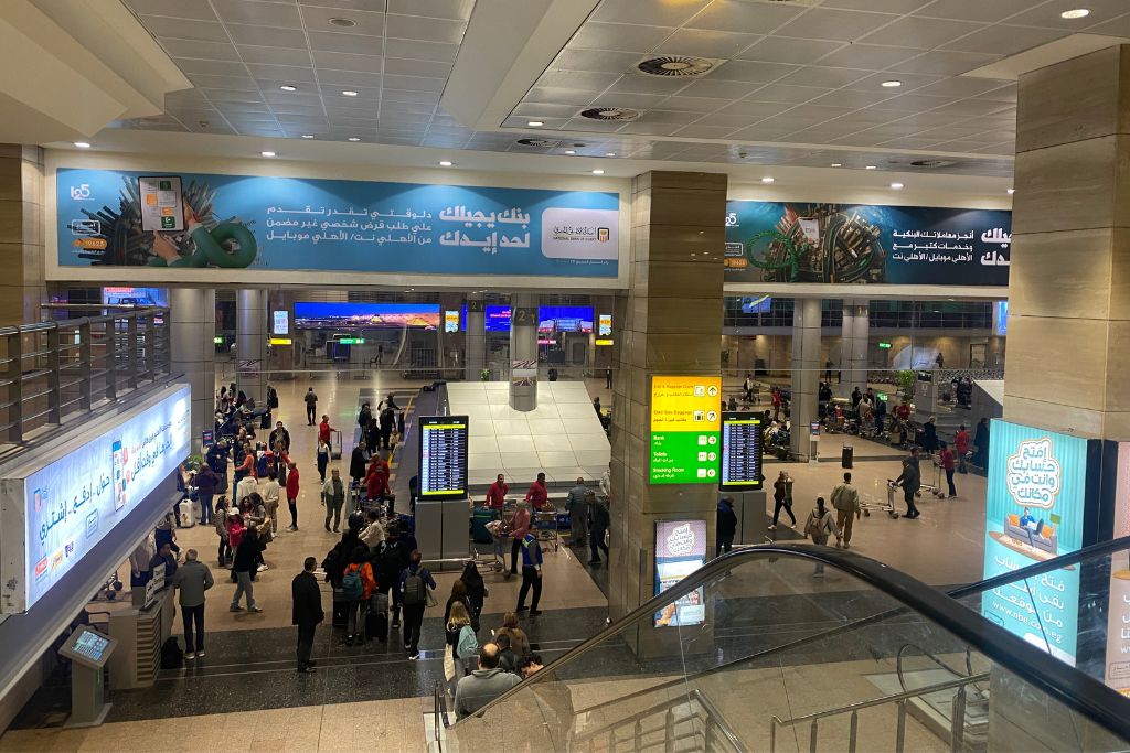 Interior view of Cairo International Airport bustling with travelers and flight information screens – helpful for Americans traveling to Egypt and those planning their arrival using the best Egypt travel tips for first-timers.