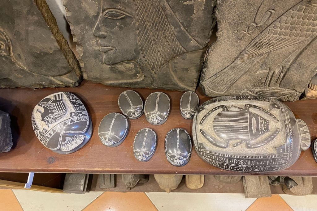 Hand-carved Egyptian scarab souvenirs displayed with ancient relief art – perfect for Egypt travel blog posts and travel tips in Egypt, including what to buy, cultural insights, and Egypt tips for first timers.