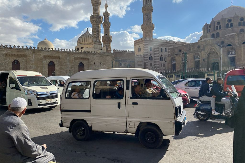 Busy Cairo street scene with a white microbus and motorbikes in front of historic mosques – ideal for travel tips for Egypt, public transportation guidance, and what to know before visiting Cairo Egypt.