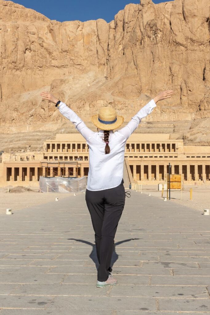 Happy solo traveler raising arms in front of the majestic Temple of Hatshepsut – perfect image for travel blogs Egypt, female solo travel Egypt inspiration, and tips for visiting Luxor temples with confidence.