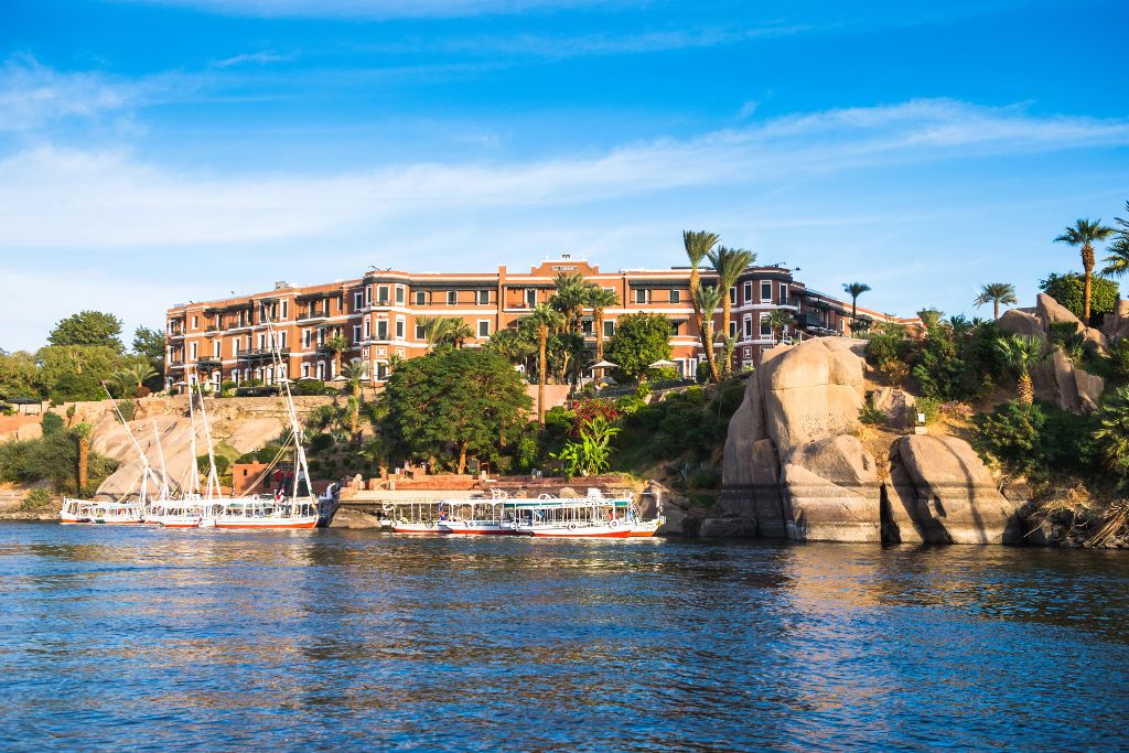 Grand view of the historic Sofitel Legend Old Cataract Hotel nestled among palm trees and rocks along the Nile River. Staying here is one of the top experiences in Egypt for couples and a true hidden gem in Egypt.