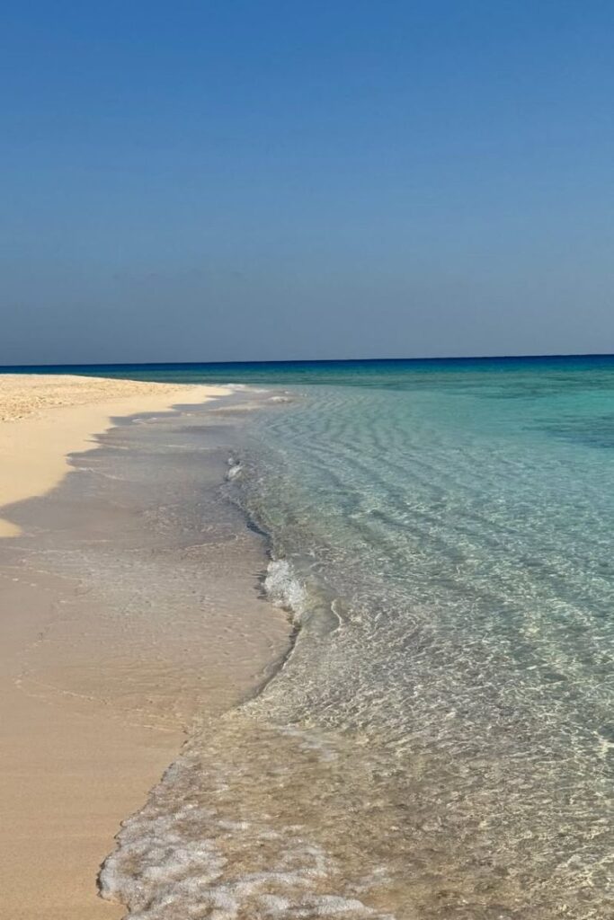 Crystal-clear water gently laps onto a sandy beach under a cloudless sky along the Red Sea coast. This peaceful setting is among the most scenic beaches in Hurghada and a must-see for anyone looking for best things to do in Hurghada Egypt.