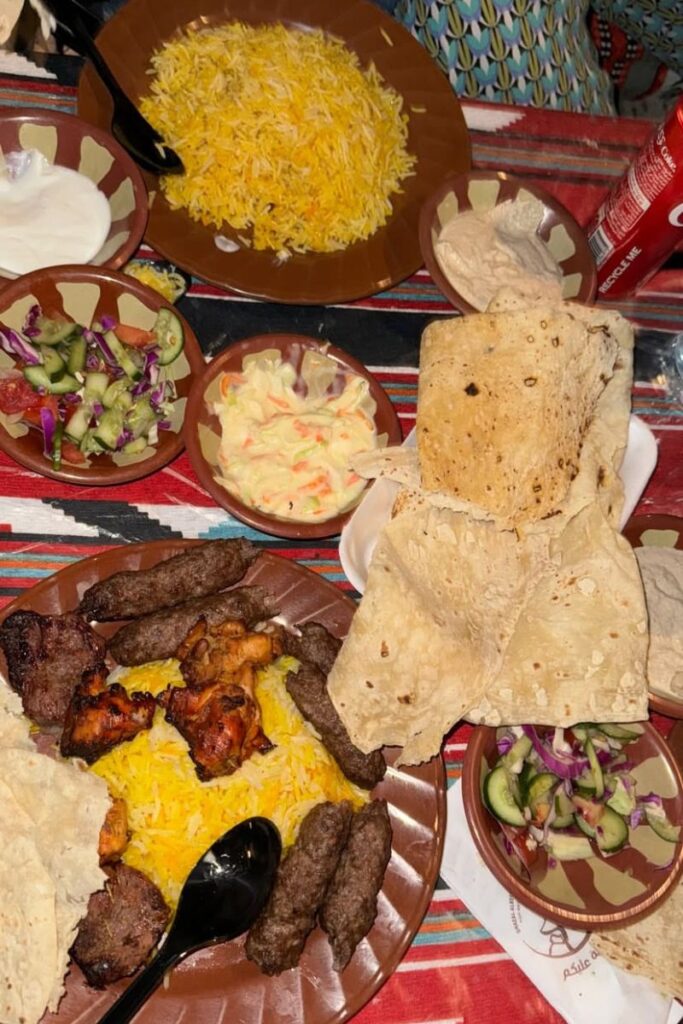A spread of grilled meats, saffron rice, fresh vegetables, flatbreads, and dips laid out on a colorful tablecloth. Sampling local cuisine is one of the top fun activities to do in Egypt and a delicious Egypt experience not to miss.