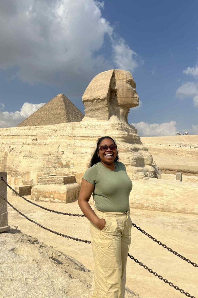 A woman poses confidently in front of the Sphinx in a fitted green t-shirt and beige cargo pants. Her practical, modest outfit shows what women wear in Egypt and matches the dress code in Egypt for sightseeing comfortably.