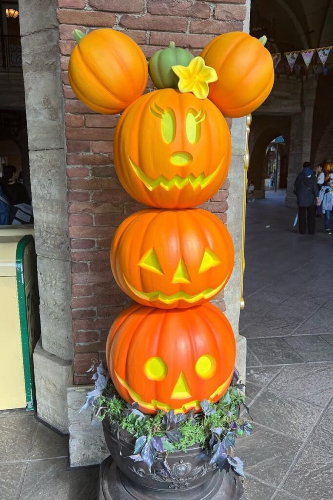 A stack of three carved pumpkins topped with Minnie Mouse ears and a flower, part of Disney’s Halloween decorations, ideal for places to visit for Halloween with kids and fun family Halloween vacations.