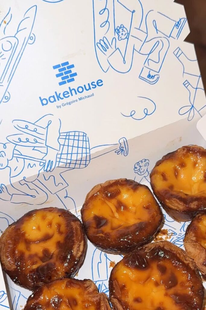 Close-up of caramelized Portuguese egg tarts from Bakehouse by Grégoire Michaud, arranged inside a white box with playful blue line illustrations. Sampling these sweet treats is one of the cool things to do in Hong Kong and a must on any Hong Kong itinerary for food lovers.