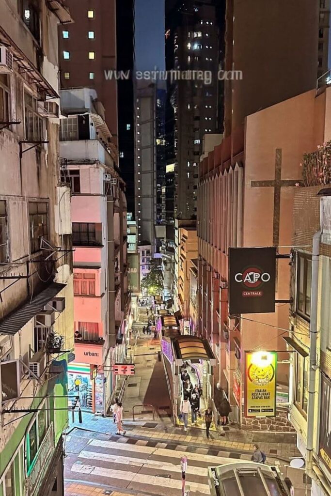 A narrow street view of Hong Kong's Mid-Levels Escalator lit up at night, surrounded by bars, shops, and apartment buildings. Exploring this area is one of the best things to do in Central Hong Kong and among the top things to do in Hong Kong at night.