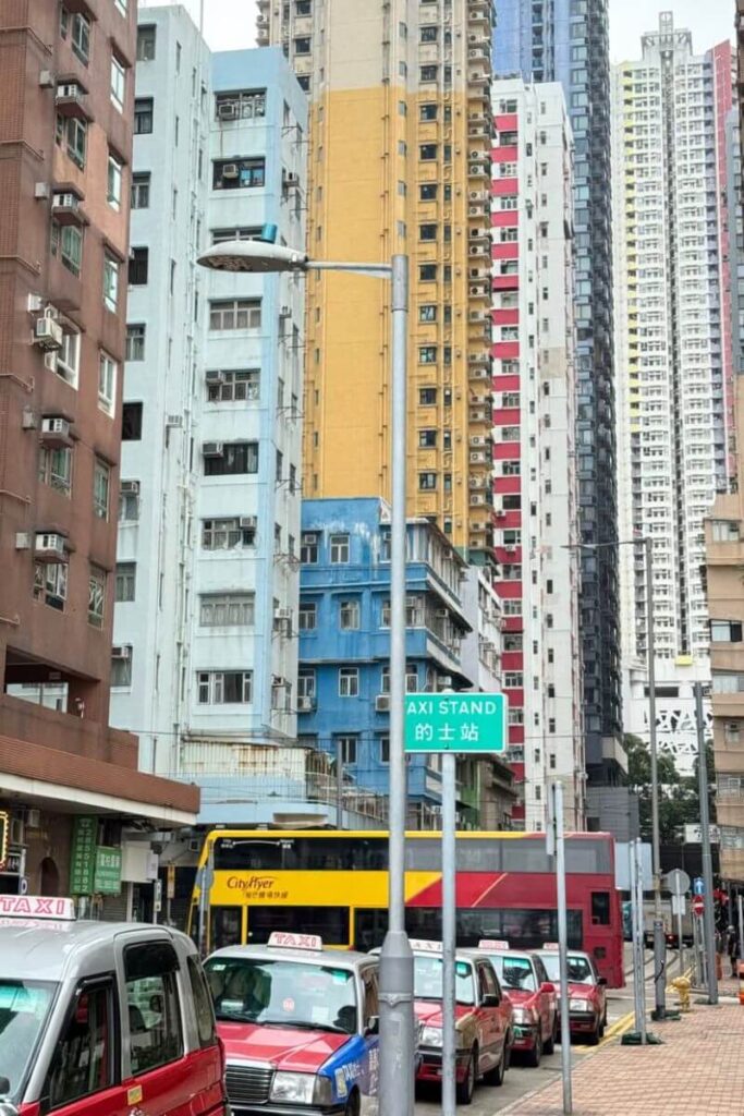 A street lined with red taxis sits below vibrant, high-rise residential buildings painted in shades of yellow, blue, and white in Kowloon. Exploring local neighborhoods like this is among the more unusual things to do in Hong Kong, especially for travelers seeking authentic activities in Hong Kong.