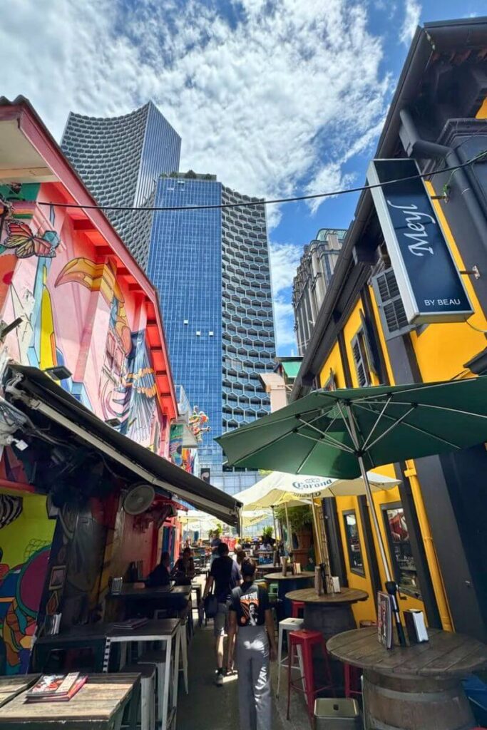 A vibrant alley in Haji Lane lined with eclectic street art, indie cafes, and boutique bars, with towering modern buildings rising behind. This is one of the best hidden gems in Singapore and a favorite for travelers seeking unique things to do in Singapore.