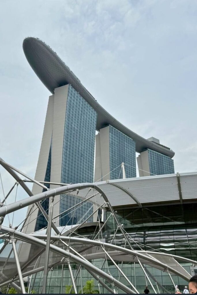 Low-angle view of Marina Bay Sands with its boat-shaped SkyPark resting atop three towers, framed by the modern lines of the Helix Bridge. This world-famous building is one of the most photographed landmarks and top attractions in Singapore.