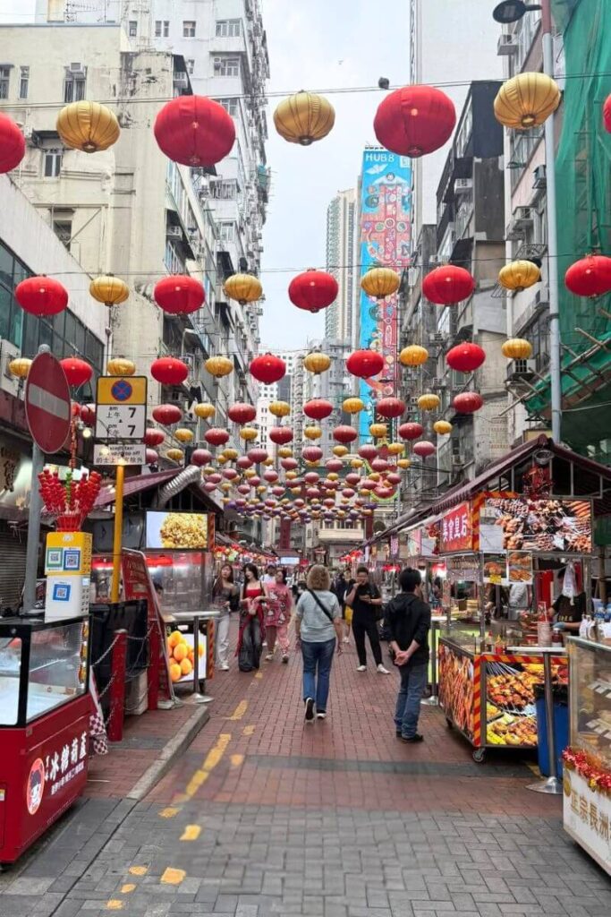 A vibrant Hong Kong street market lined with red and gold lanterns, food stalls, and visitors browsing snacks. Exploring night markets is one of the essential things to know before going to Hong Kong for authentic street food.