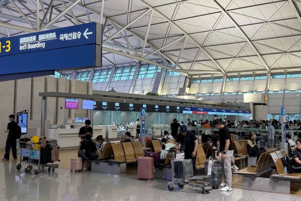 Travelers wait with luggage in a bright, modern international boarding terminal at Hong Kong International Airport. A key travel advisory for Hong Kong is to arrive early, as this airport is one of the busiest in Asia.