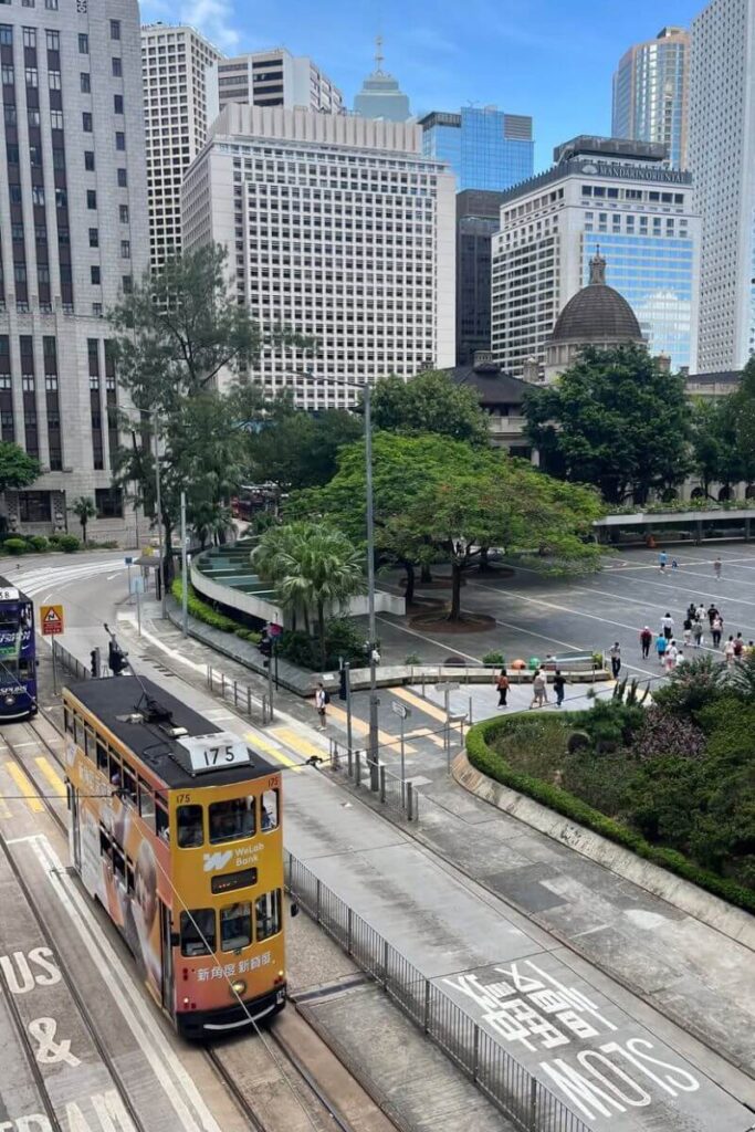 A double-decker tram passing through Central Hong Kong with modern skyscrapers and historic buildings in the background. A classic scene when comparing Hong Kong vs Singapore transport.