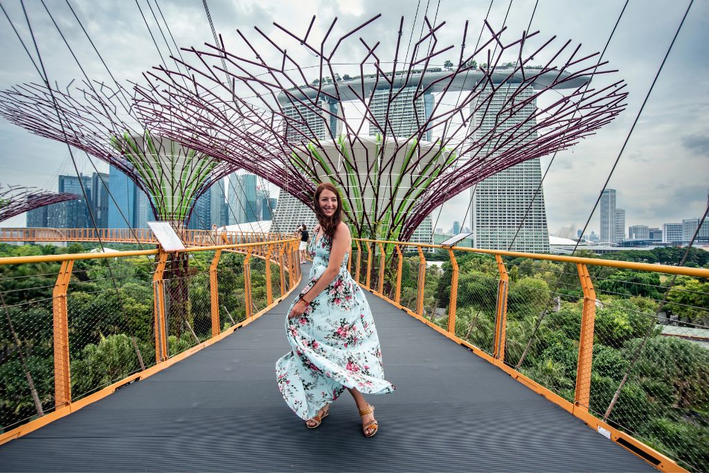 A traveler in a floral dress walking along the OCBC Skyway at Gardens by the Bay, with Marina Bay Sands rising behind. A must-visit highlight for Singapore vs Hong Kong trips.