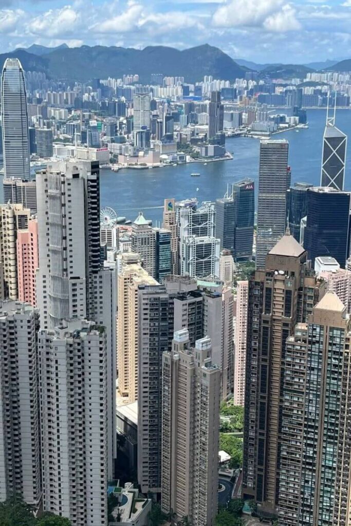 A sweeping view of Hong Kong’s dense skyline and Victoria Harbour, framed by tall skyscrapers and distant mountains. An iconic cityscape for any Hong Kong or Singapore comparison.
