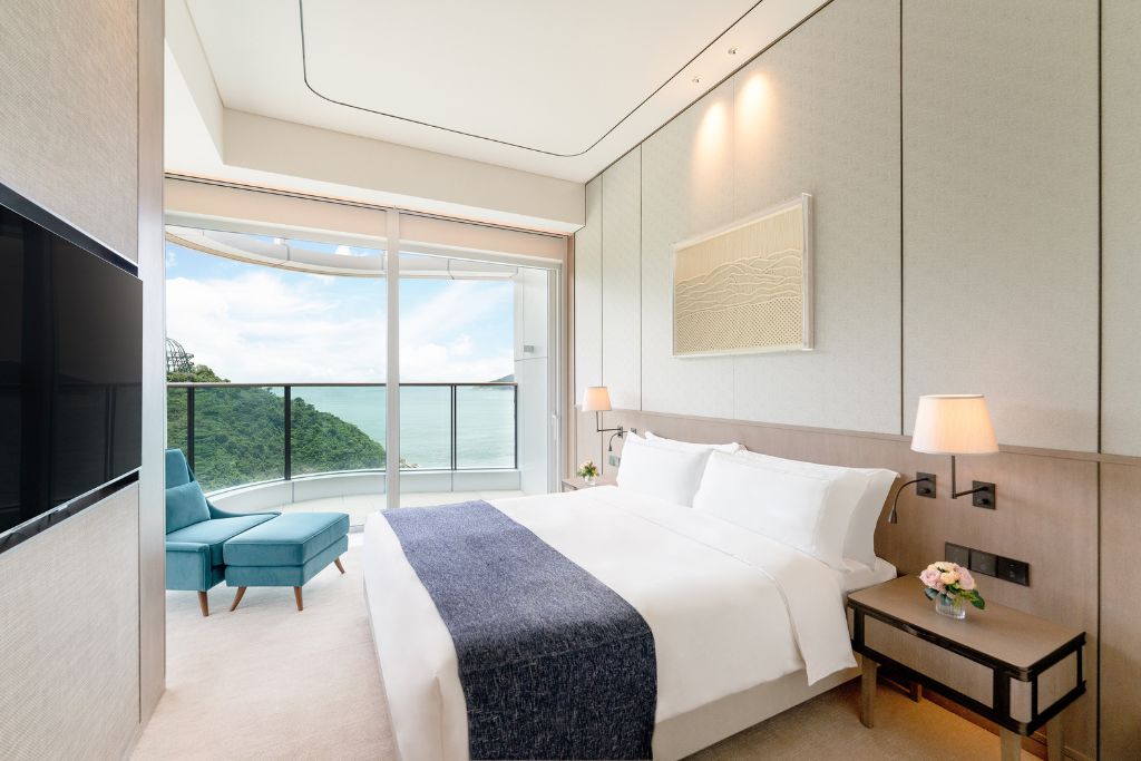 Bright, modern hotel bedroom in Hong Kong with large windows showing ocean views and lush hills. Choosing hotels with scenic views is one of the best Hong Kong tips and tricks for a comfortable stay.