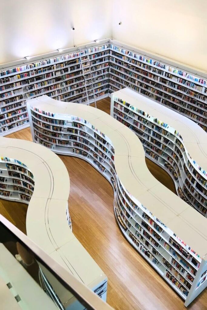 Top-down view of the sleek, modern interior of Library@Orchard, showcasing curving white bookshelves filled with books under bright lighting. This visually stunning space is perfect for book lovers and one of the best indoor things to do in Singapore for free.