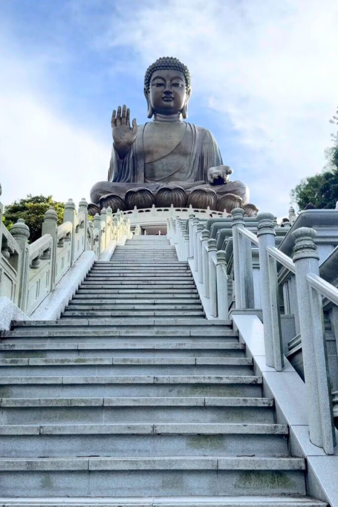 A grand staircase leading up to the Tian Tan Buddha, surrounded by white stone railings and blue skies. A spiritual must-visit when choosing Hong Kong or Singapore.