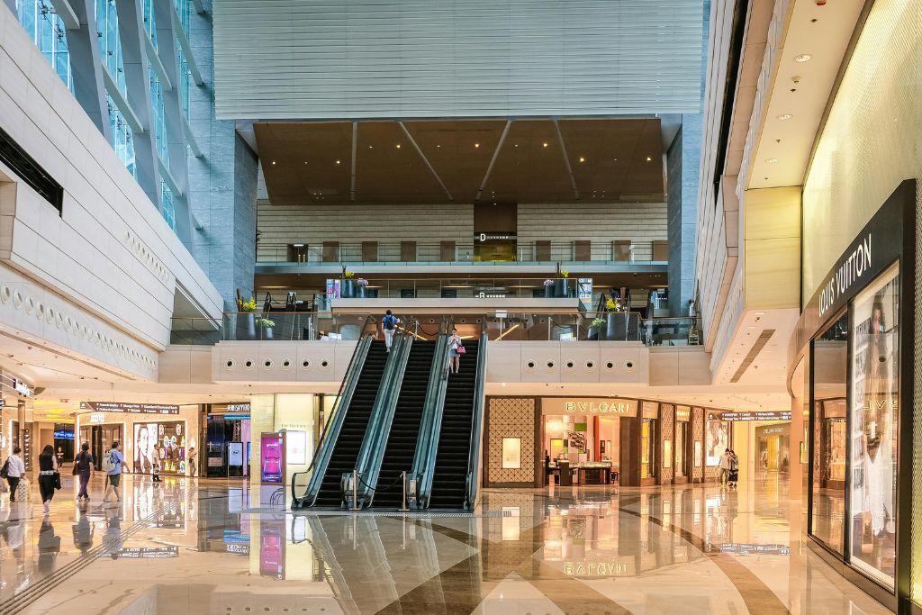 An upscale mall interior with shiny floors, escalators, and luxury storefronts like Louis Vuitton and Bvlgari, reflecting a sleek and modern shopping experience. Exploring malls is one of the cool things to do in Hong Kong during a layover or while waiting at the Hong Kong airport.